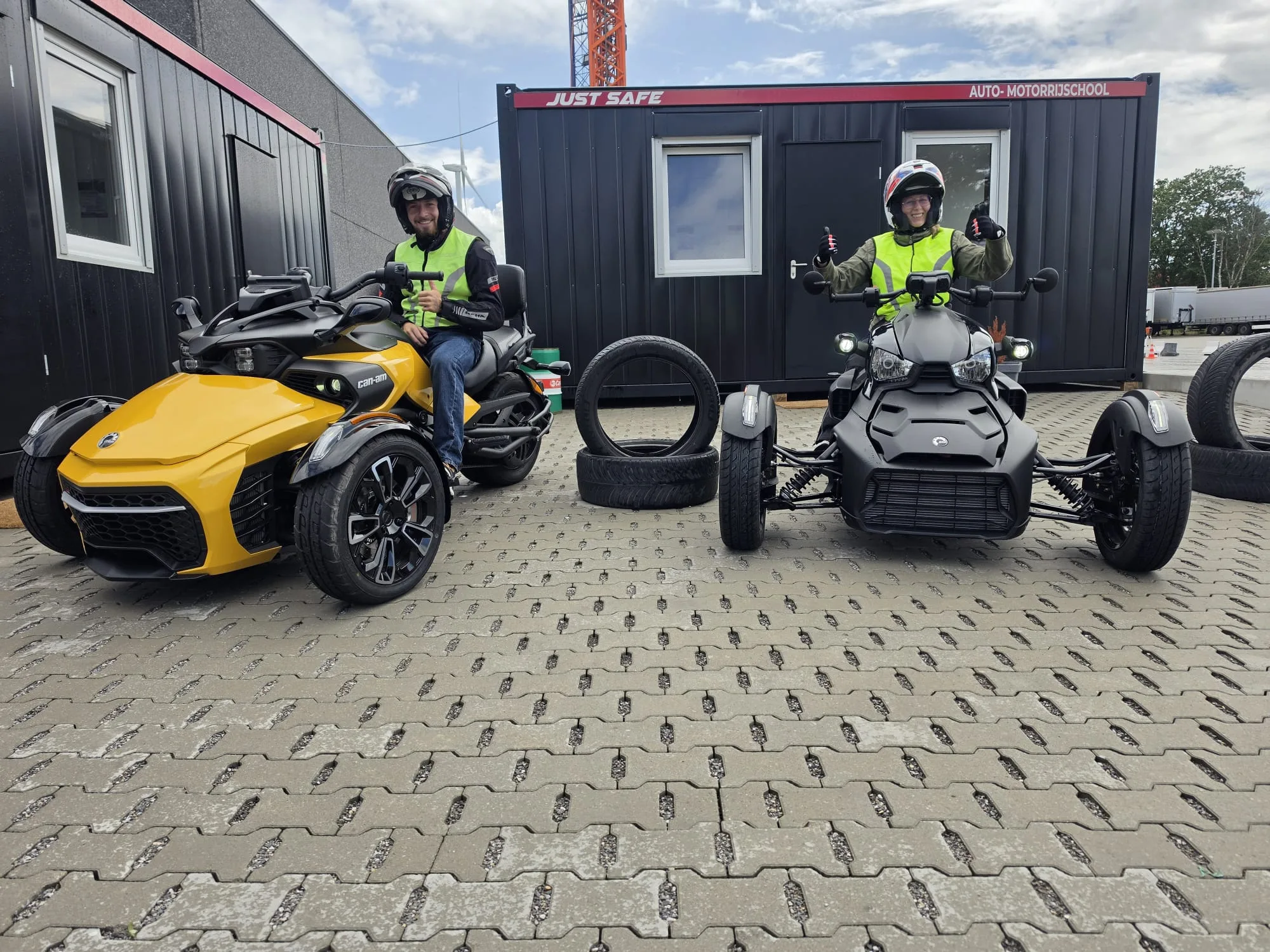 Twee leerlingen met duim omhoog op een gele en een zwarte Can-Am driewieler (code 373) bij de vestiging in Tessenderlo